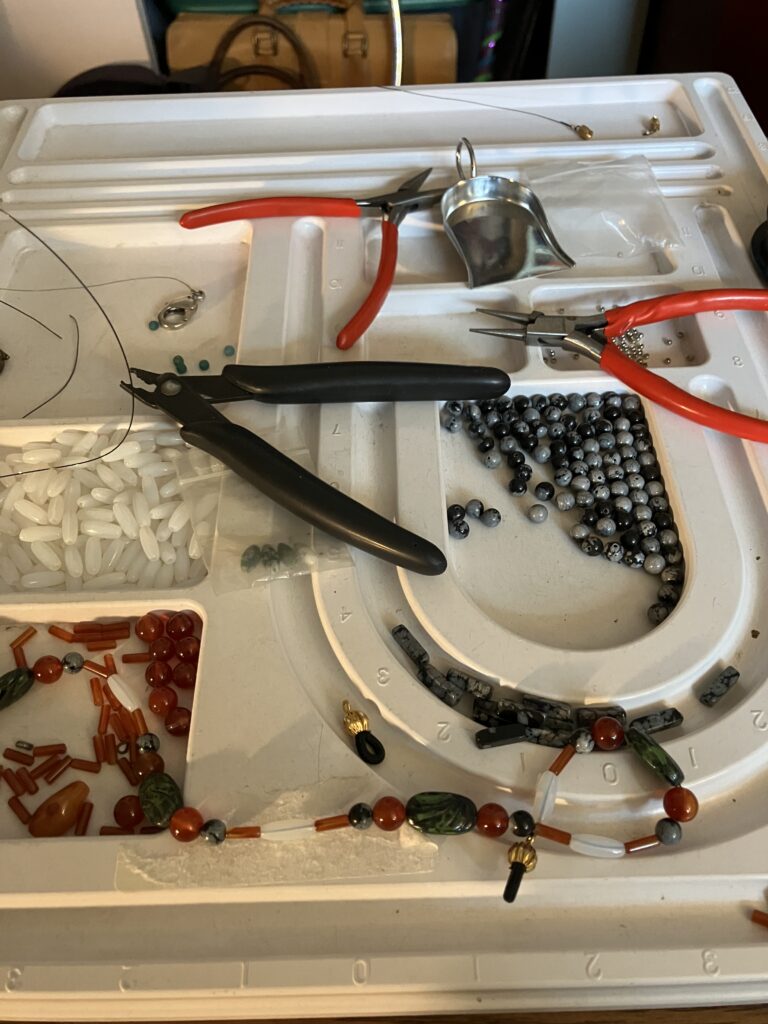 Beading board with beading tools, beads, and a completed glasses chain on the perimeter of the board